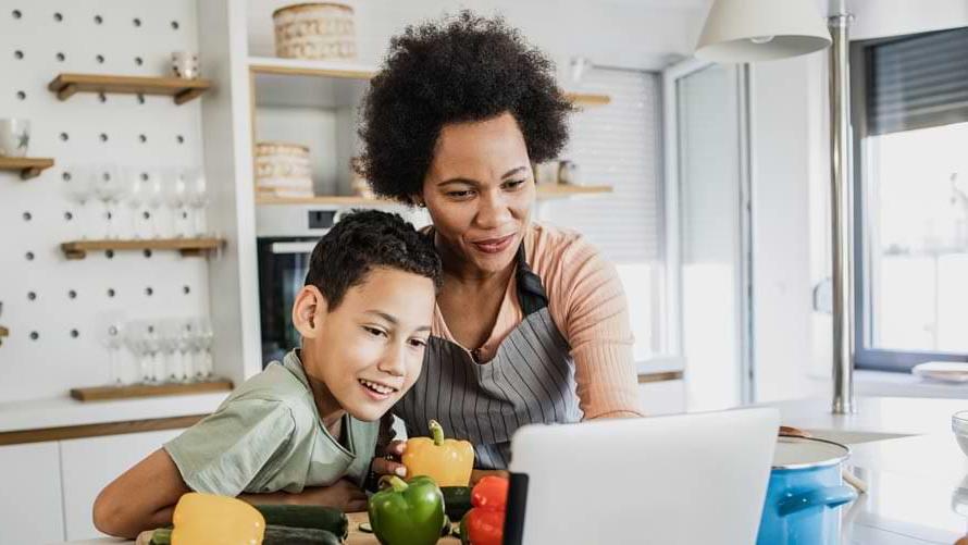 一个小男孩和他的母亲在厨房里根据平板电脑上的食谱准备食物